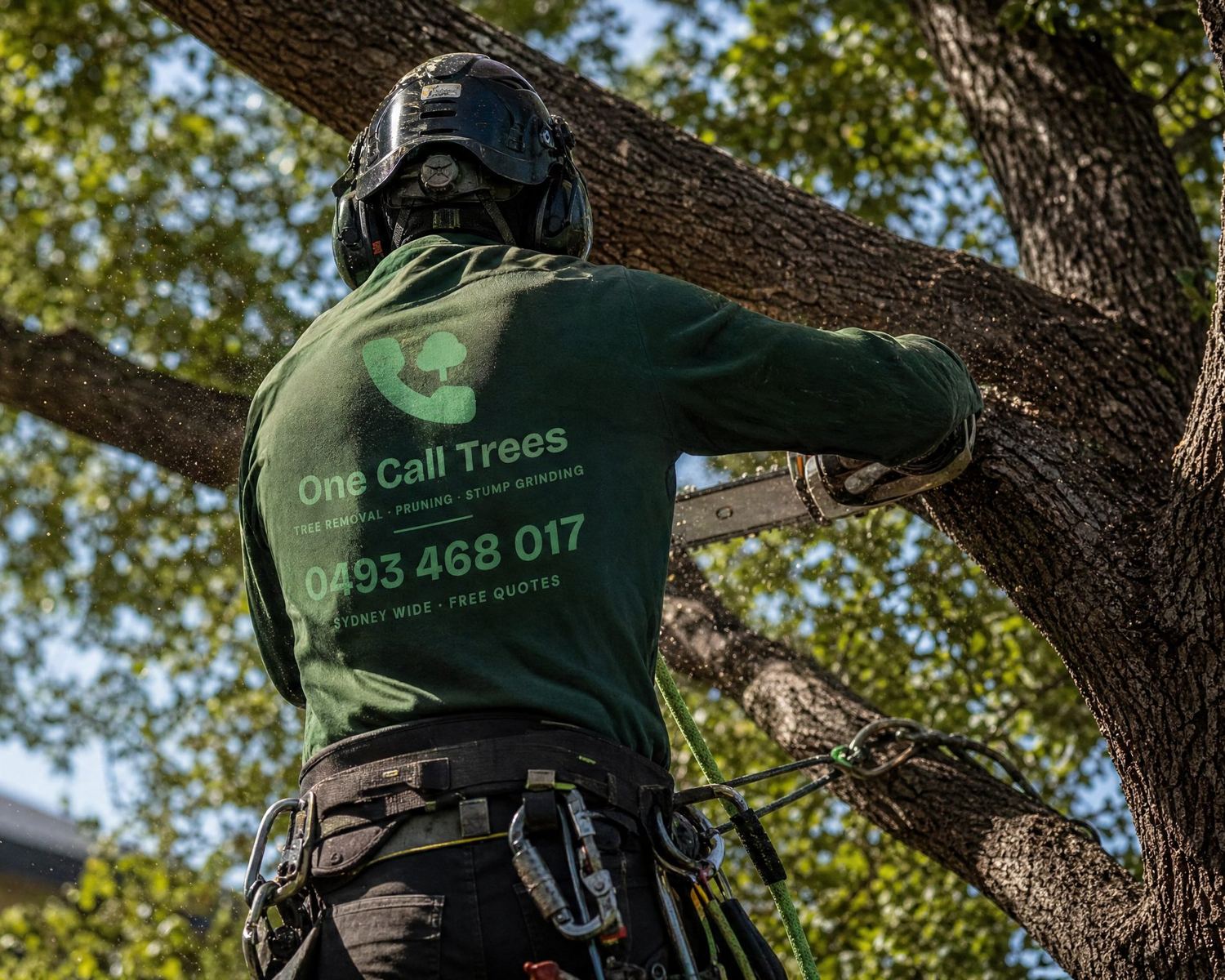 One Call Trees arborist in a climbing harness cutting a large branch with a chainsaw